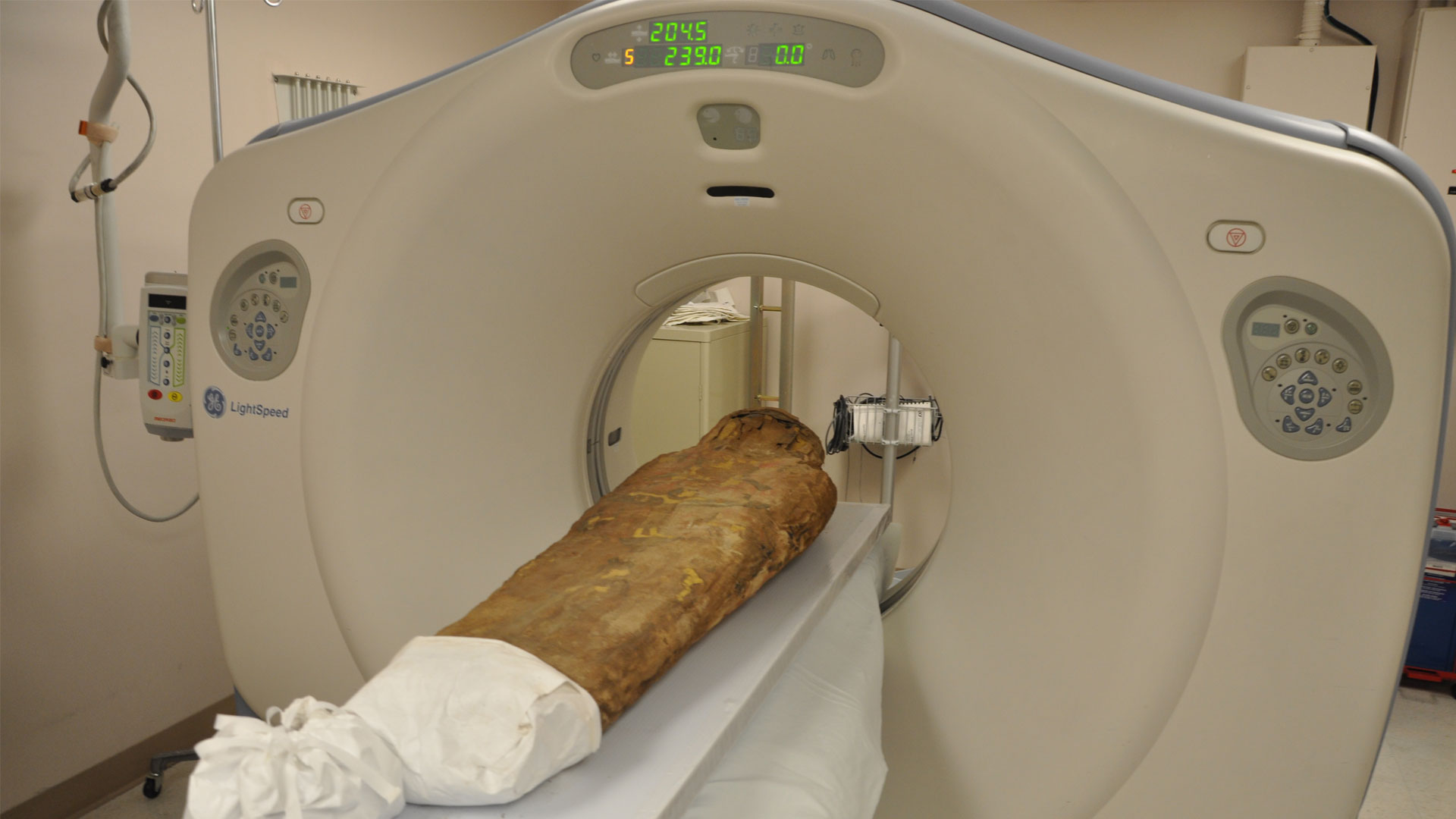 mummy on a board going through a modern CT scan machine