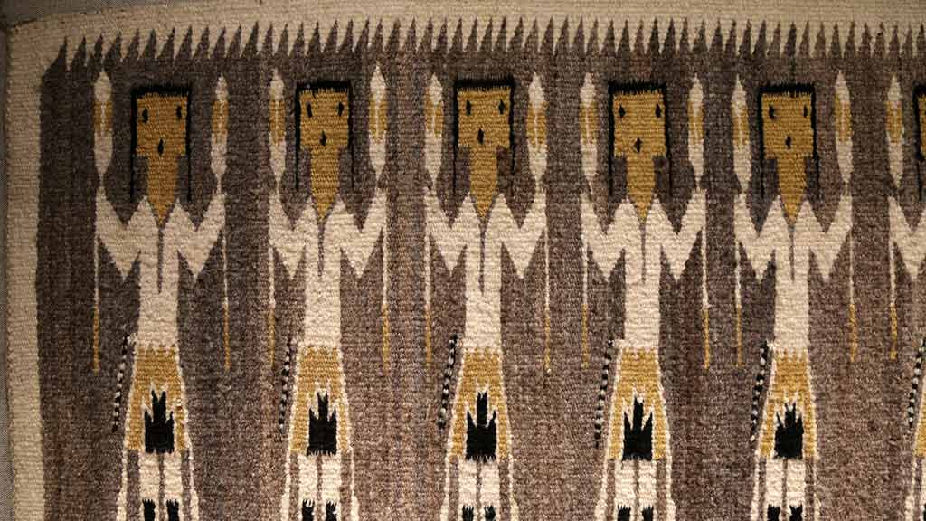 rug with repeated design of people holding long objects that look like torches